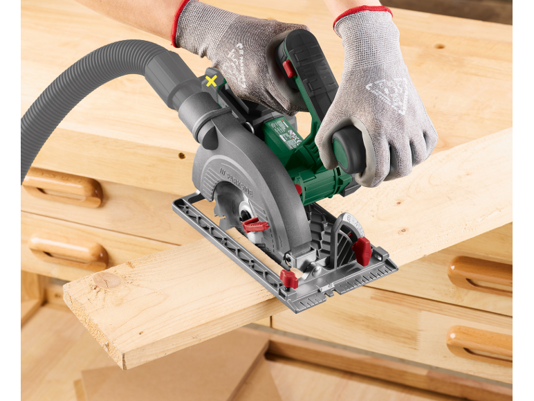 Person cutting a wooden board with a circular saw, connected to a dust extraction hose.