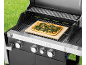 Gas barbecue with a rectangular vegetable pizza on a baking stone, with grass in the background.