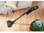 Blue cordless vacuum cleaner on wooden floor, with sofa and plant.