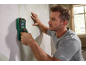 Man using a wall detector on a wallpapered wall.