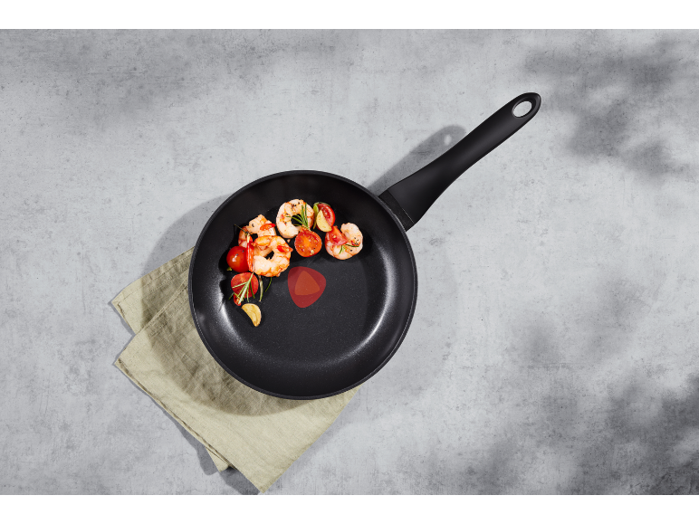 Shrimp and cherry tomatoes in a black frying pan on a grey kitchen towel.