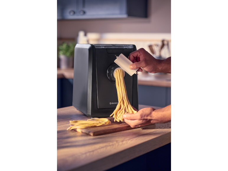 A person making fresh pasta with a black pasta machine in a kitchen.