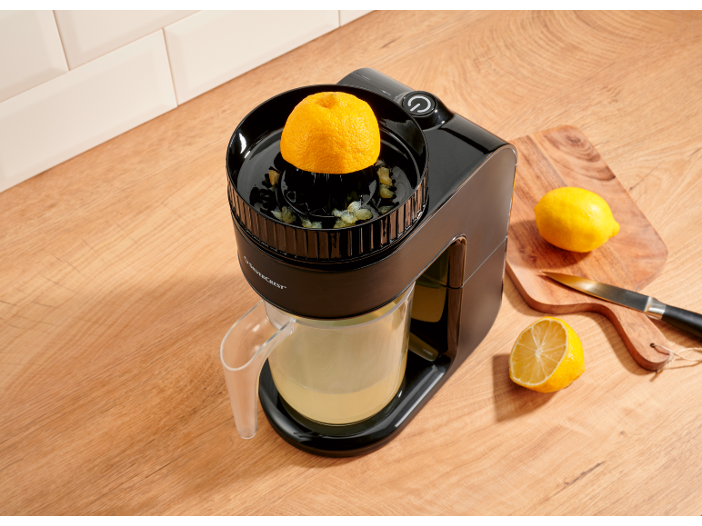 Black electric citrus juicer with a squeezed orange and lemons on a wooden cutting board.