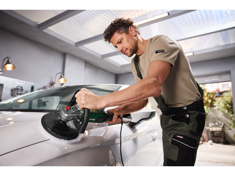 Man polishing a white car with an electric polisher in a garage.