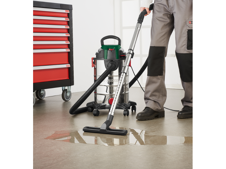 Wet and dry vacuum cleaner with stainless steel tank, cleaning a puddle of water from the floor.