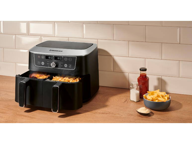 Black dual-basket air fryer with fries and chicken on a wooden surface.