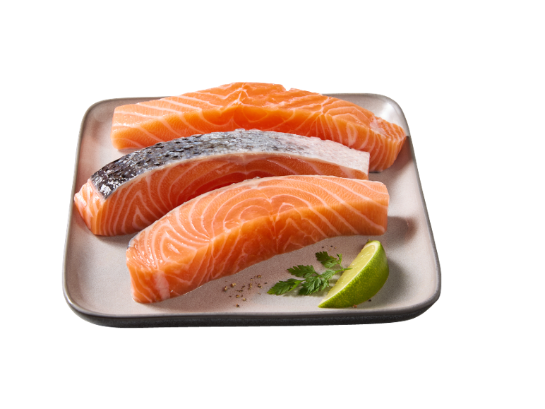 Three pieces of fresh salmon with skin, a lime wedge, and parsley on a plate.