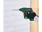 Green and black hammer drill drilling into a white brick wall.