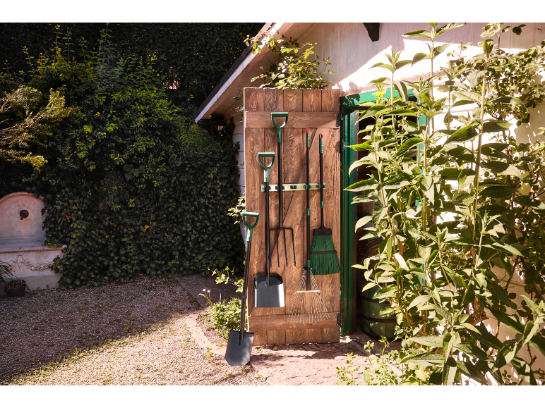 Gardening tools hanging on a wooden door, with a shovel and rake in the foreground.