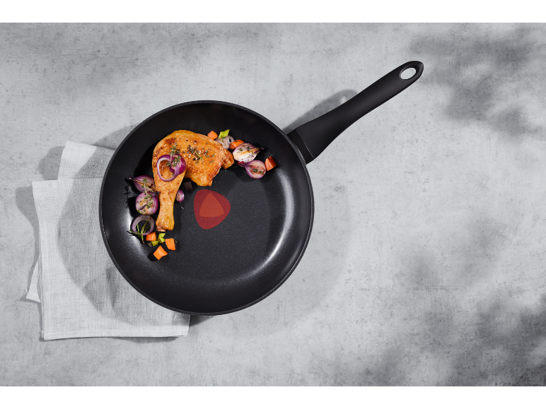 Frying pan with roasted chicken leg, onion, and carrot on a kitchen towel.