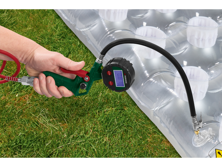 Handheld air pump with pressure gauge inflating an inflatable mattress on grass.