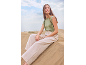 Woman in a green sleeveless top and beige trousers sitting on a sand dune.
