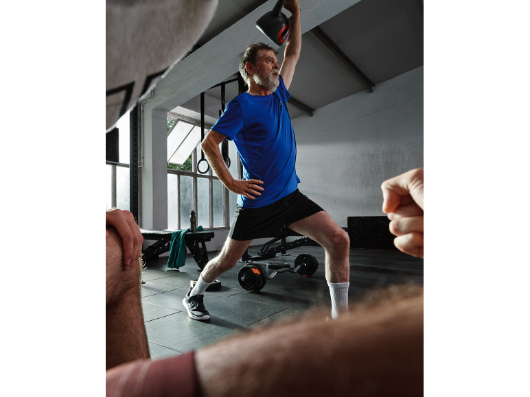 Man in blue t-shirt and black shorts lifting a kettlebell in a gym.