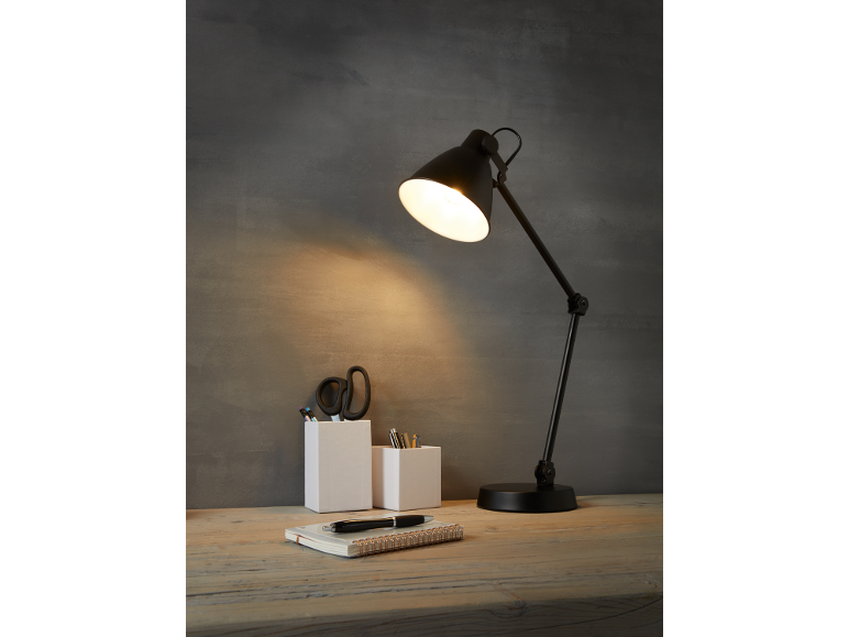 Desk lamp illuminating a wooden table with pen organizers and a notebook.