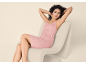 Woman in pink slip dress sitting in a cream armchair.