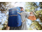 Man with blue cooler backpack drinking water in a sunny forest.