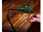 Illuminated magnifying glass on flexible stand, small parts, and hands on a wooden table.