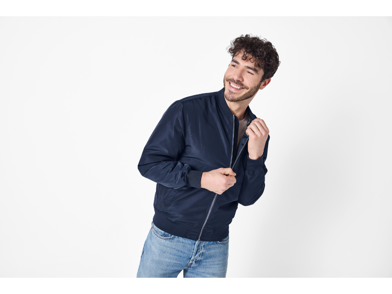 Smiling man in a dark blue bomber jacket and jeans.