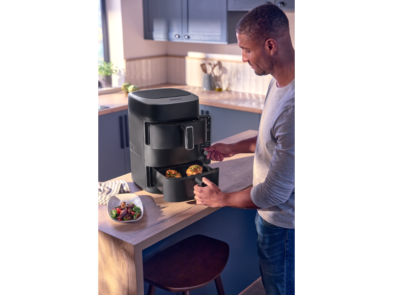 Man in kitchen using a black dual drawer air fryer.
