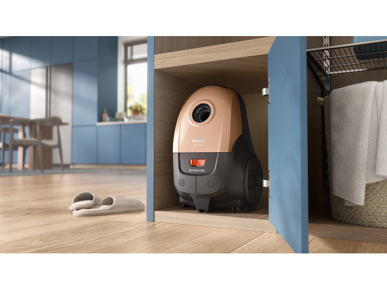Compact vacuum cleaner in a wooden cabinet, with slippers on the floor of a modern kitchen.