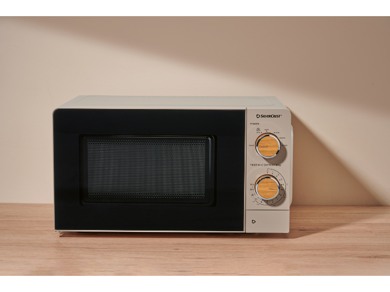 Beige microwave with control panel featuring wooden rotary knobs, on a wooden table.