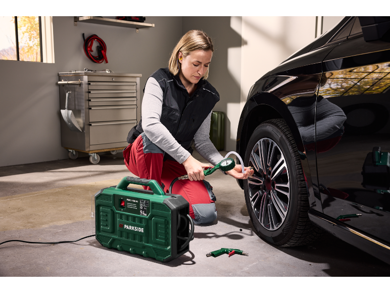 A woman inflates a car tire with a portable compressor in a garage.