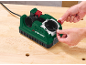 Male hands inserting a drill bit into a drill sharpener on a wooden table.