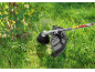 A grass trimmer cuts grass around a bush, creating water splashes.
