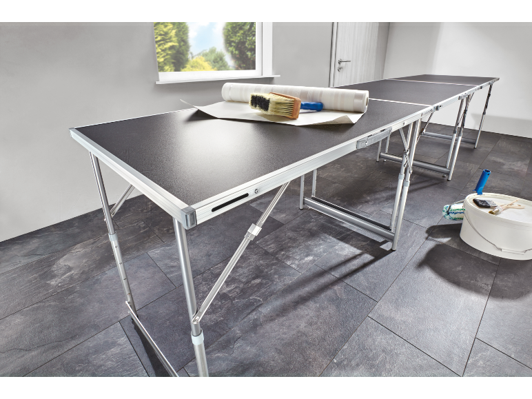 Folding wallpapering tables with tools and a bucket in a room.