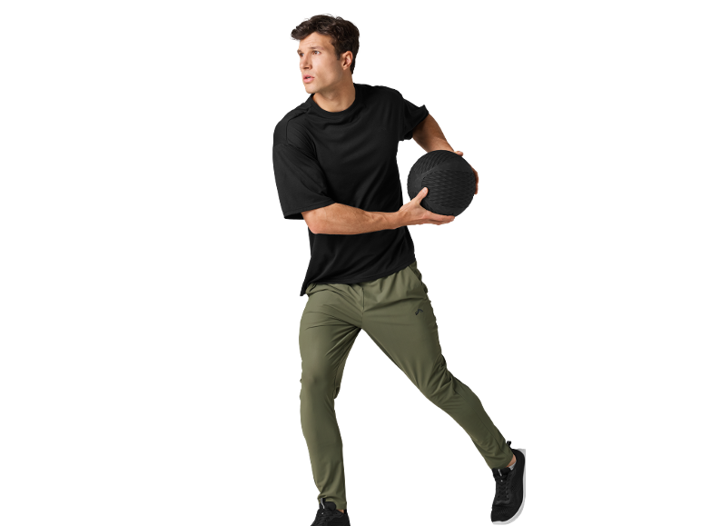 Man in black t-shirt and green trousers holding a medicine ball.