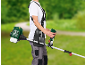 Person with a petrol brush cutter against a blurred green landscape background.
