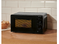 Black microwave oven on a wooden countertop with tiled background and a basket of bread.