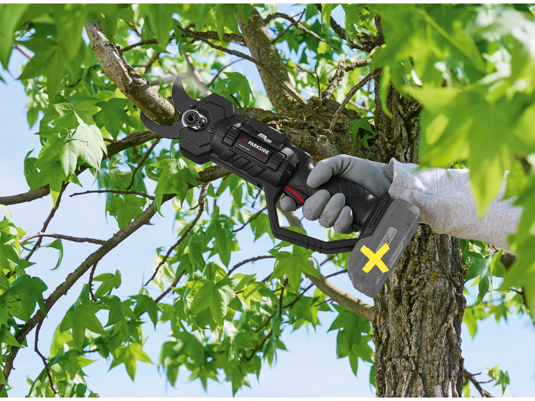 Cordless pruning shears cutting a tree branch, green leaves visible.