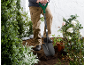 Person digging soil with a shovel in a garden with plants and roses.