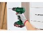 Man with glove holding a cordless drill, drilling a hole into a white cabinet.