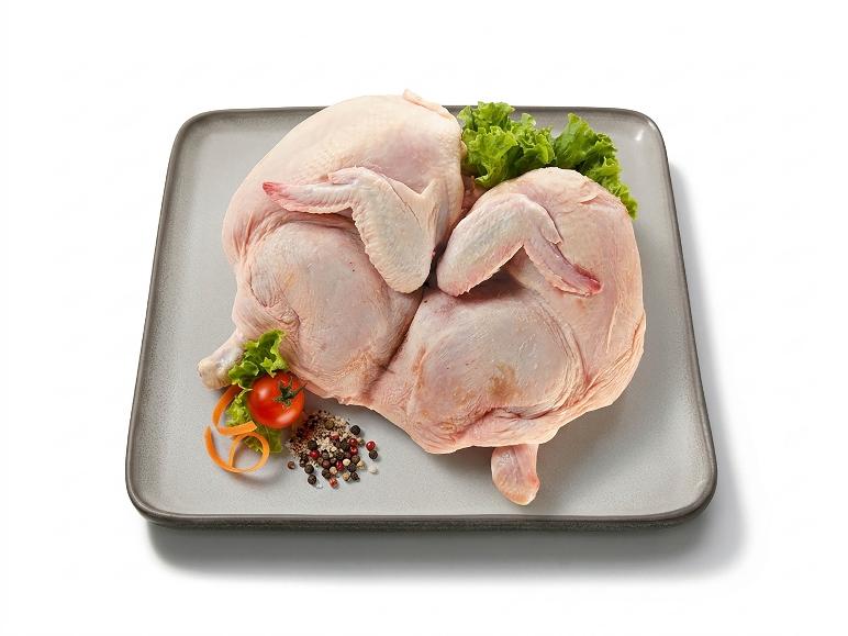 Two whole raw chickens with spices and vegetables on a gray tray.