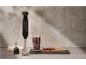 Black hand blender with attachments and berries in a measuring cup on a kitchen counter.