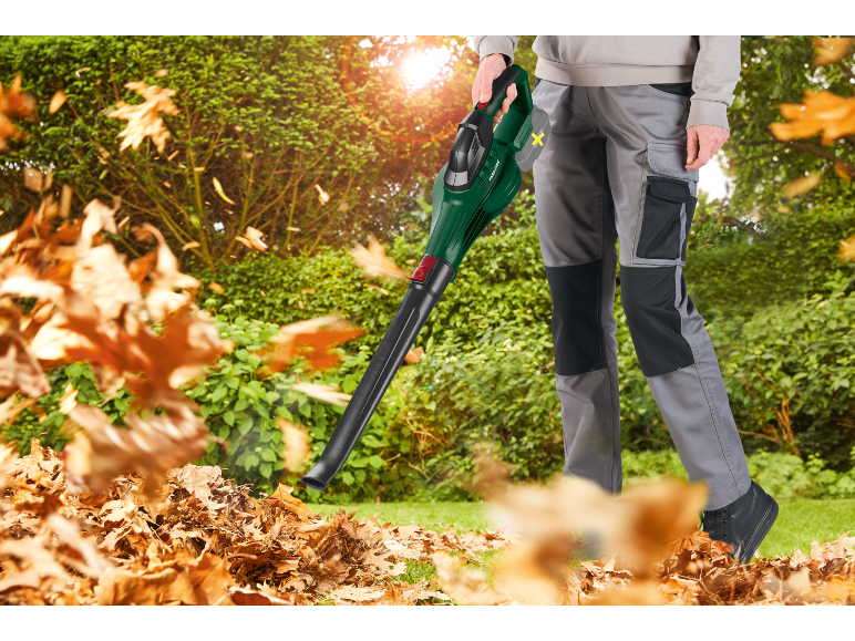 Man with electric leaf blower clearing dry leaves in the garden.