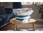 Folded laundry in a blue and white collapsible basket on a wooden table in a living room.