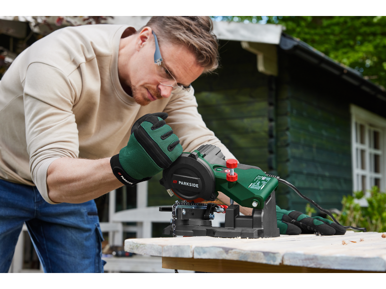 A man uses a Parkside chain saw sharpener outdoors.
