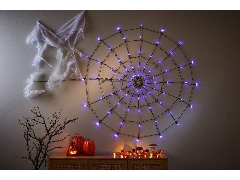 Spider web with purple lights, cobwebs, and Halloween pumpkins on a dresser.