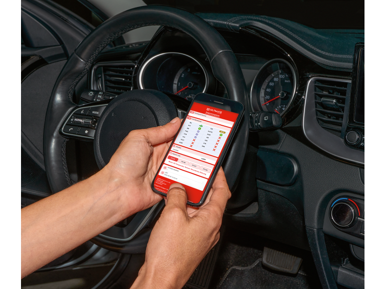 A person in a car holds a smartphone with a car diagnostic application.