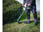Man using a cordless grass trimmer on a lawn by a bush.