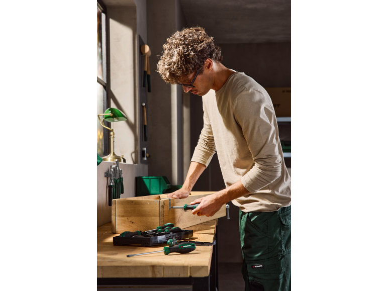 Man assembling a wooden box with a screwdriver in a workshop.