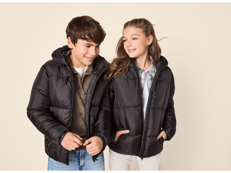 Two smiling children wear black hooded puffer jackets, one with a brown sweater and the other with a plaid shirt.