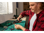 Man with crimping pliers and wires working on an electronics project on a green mat.