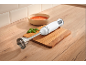 Immersion blender on a wooden board next to a bowl of tomato soup and basil.