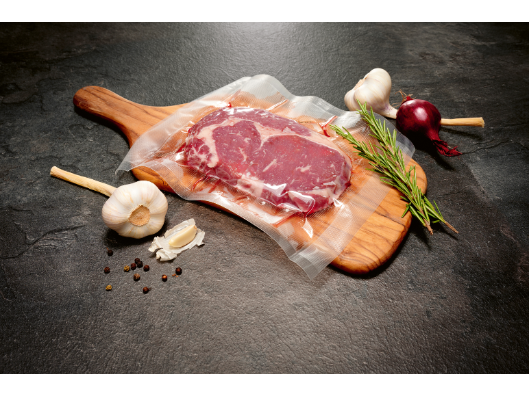 Vacuum-sealed steak on a board with garlic, rosemary, and onion.
