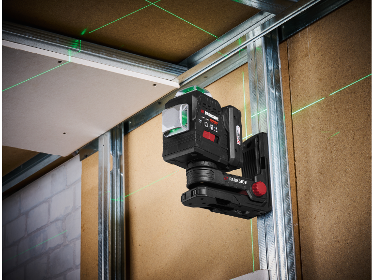 Laser level mounted on a metal frame, projecting green laser lines onto walls and ceiling.