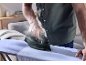 A person ironing a light blue shirt on an ironing board with a dark iron.